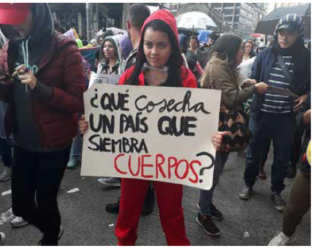 Mujer en la marcha del 21 de noviembre, en la carrera séptima de Bogotá, con un cartel que dice: "Qué cosecha un país que siembra cuerpos?"